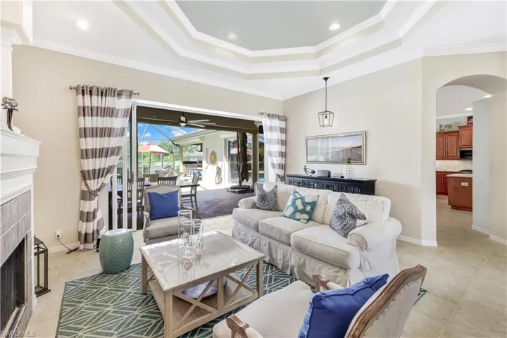 Tiled living room featuring a tiled fireplace, crown molding, a tray ceiling, and ceiling fan