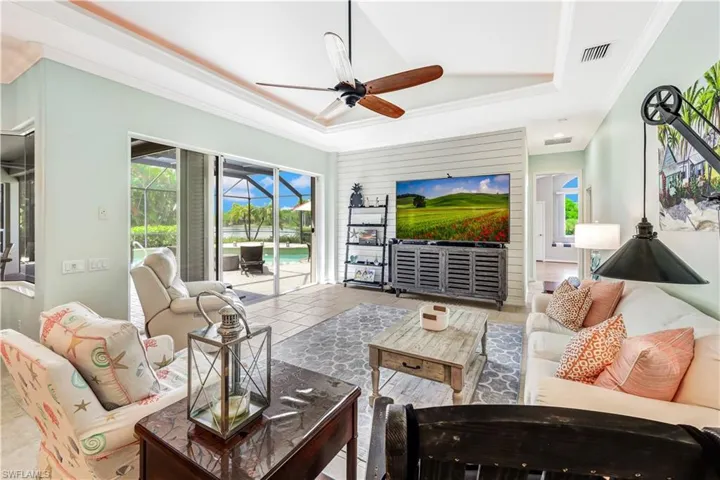 Tiled living room featuring ornamental molding, a healthy amount of sunlight, ceiling fan, and a raised ceiling