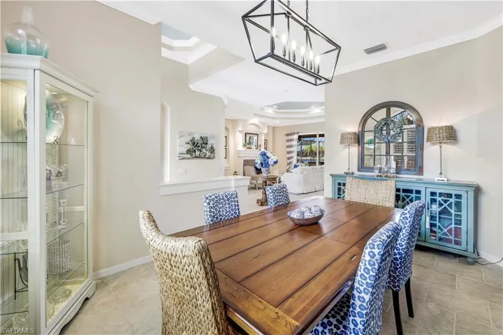 Dining area with crown molding, an inviting chandelier, a tray ceiling, and light tile patterned floors