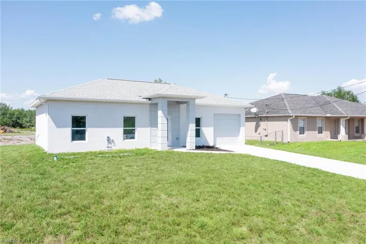 Prairie-style home with an attached garage, driveway, stucco siding, and a front yard