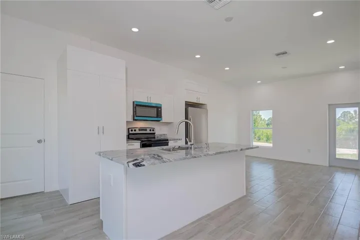 Kitchen with visible vents, a sink, an island with sink, white cabinetry, and stainless steel appliances