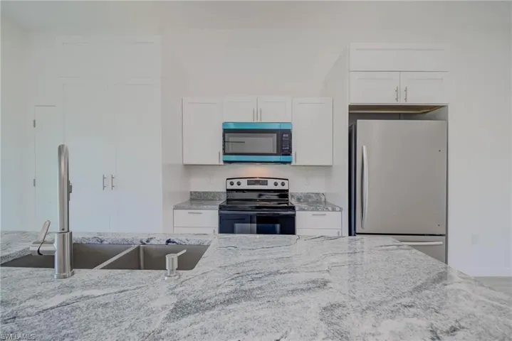 Kitchen with stainless steel appliances, white cabinetry, a sink, and light stone counters