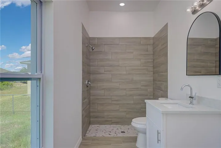 Full bath featuring toilet, tiled shower, and vanity