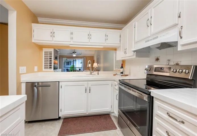 Kitchen featuring backsplash, light tile patterned floors, custom range hood, appliances with stainless steel finishes, and ceiling fan