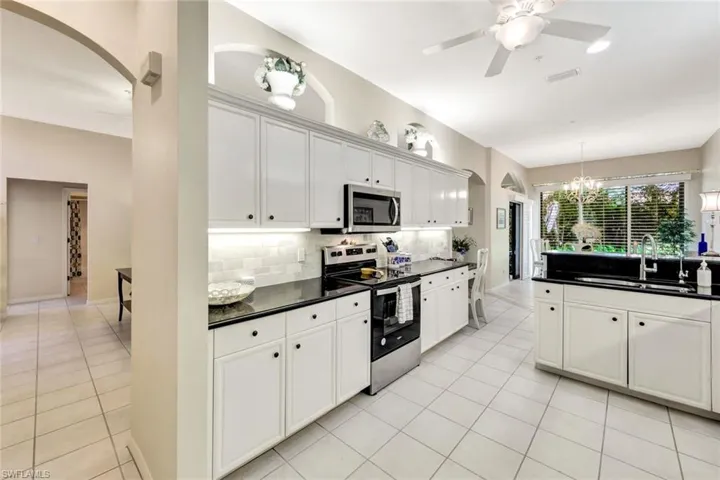 Kitchen featuring a sink, appliances with stainless steel finishes, light tile patterned floors, dark countertops, and arched walkways