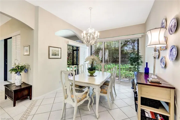 Dining space featuring vaulted ceiling, baseboards, light tile patterned flooring, arched walkways, and a notable chandelier