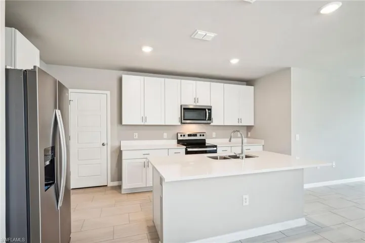 Kitchen featuring an island with sink, sink, stainless steel appliances, and white cabinets