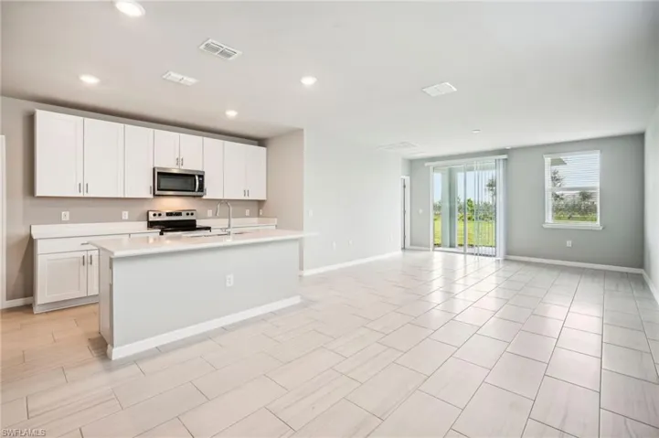 Kitchen with a kitchen island with sink, sink, stainless steel appliances, and white cabinets