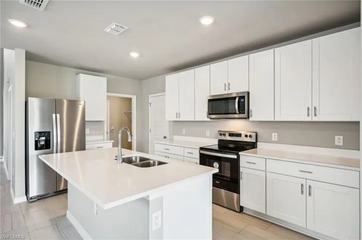 Kitchen with stainless steel appliances, white cabinets, a kitchen island with sink, and sink