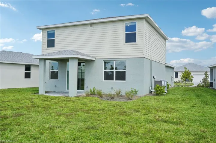 Back of property with a garage, central AC unit, and a yard