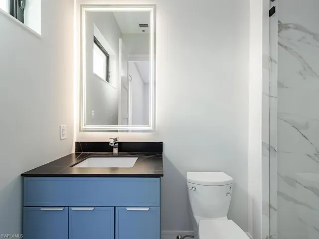 Bathroom with a marble finish shower, vanity, and toilet