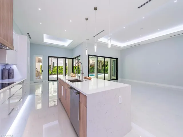 Kitchen with a spacious island, a raised ceiling, hanging light fixtures, stainless steel dishwasher, and modern cabinets