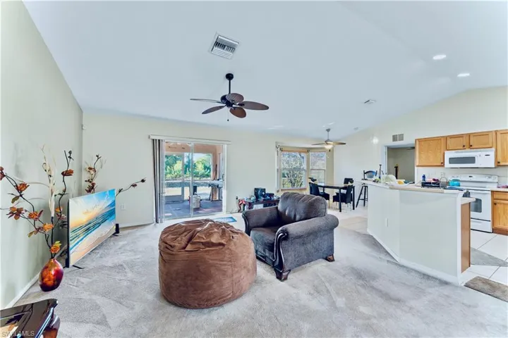 Living area with light colored carpet, lofted ceiling, a ceiling fan, and visible vents