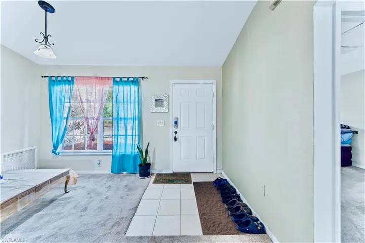 Carpeted foyer featuring tile patterned floors, visible vents, baseboards, and lofted ceiling