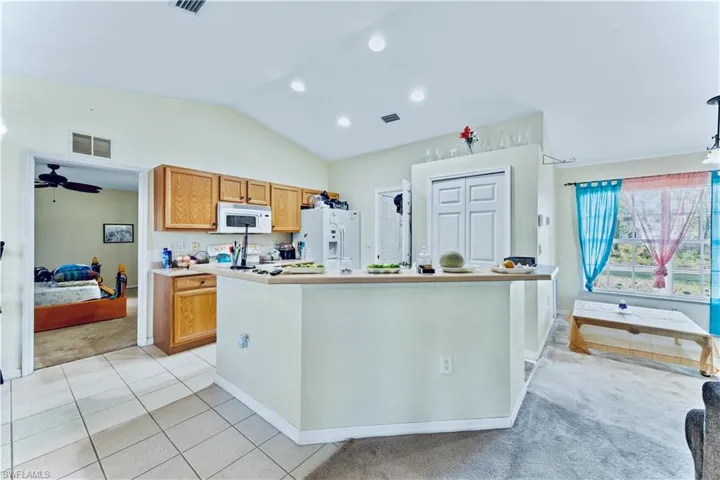 Kitchen featuring visible vents, light countertops, lofted ceiling, light tile patterned flooring, and white appliances