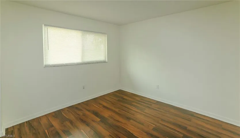 Wood-finish flooring with white wall finishes and a window featuring horizontal blinds