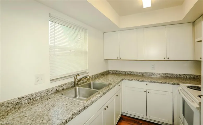 White cabinetry with chrome pulls, dual basin stainless steel sink, granite-style countertops, and wood-finish flooring