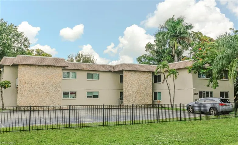 Two-story building featuring stucco exterior with stone accents, a shingle roof, and a black metal fence