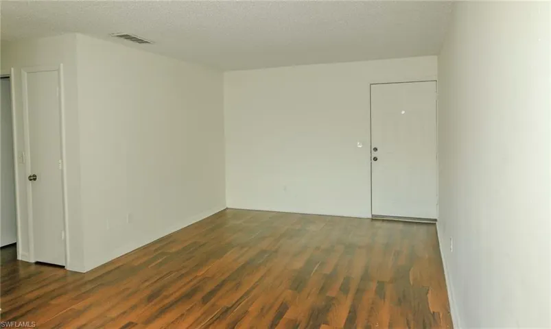 Wood-finish flooring, white painted walls, and a textured ceiling