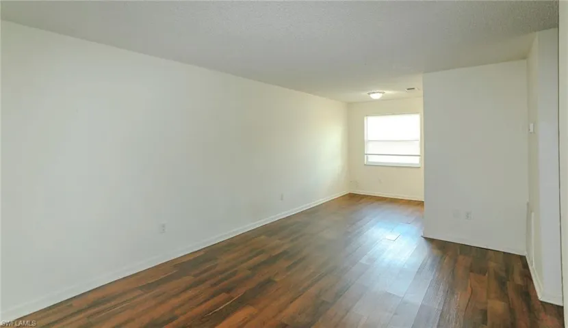 Spacious room featuring wood-finish flooring, white walls, and a ceiling-mounted light fixture