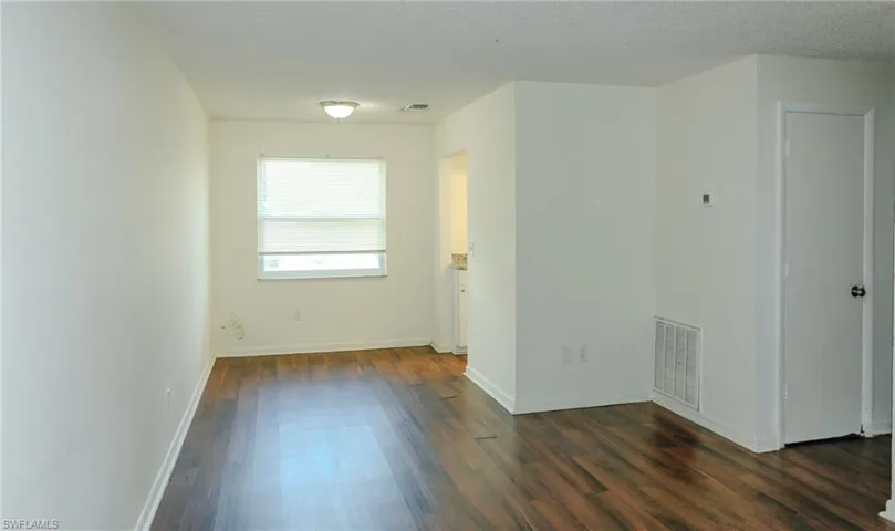 Spacious interior with wood-finish flooring, white walls, and a window with blinds