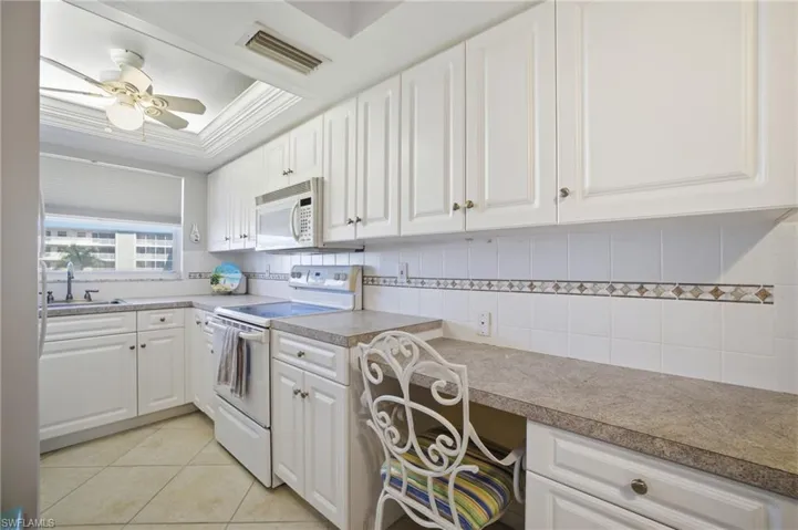 Kitchen featuring white cabinetry, white appliances, decorative backsplash, a raised ceiling, and light tile patterned floors