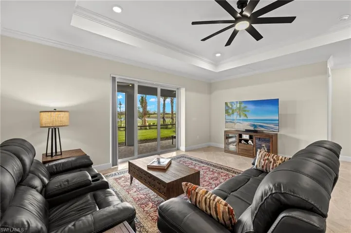 Living room featuring a ceiling fan, a raised ceiling, baseboards, and ornamental molding