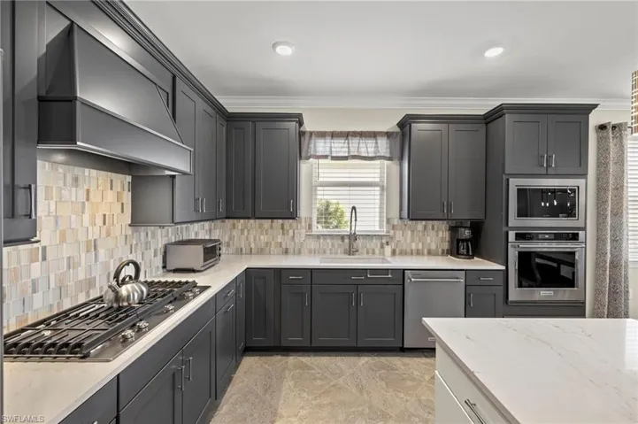 Kitchen featuring premium range hood, stainless steel appliances, ornamental molding, and a sink