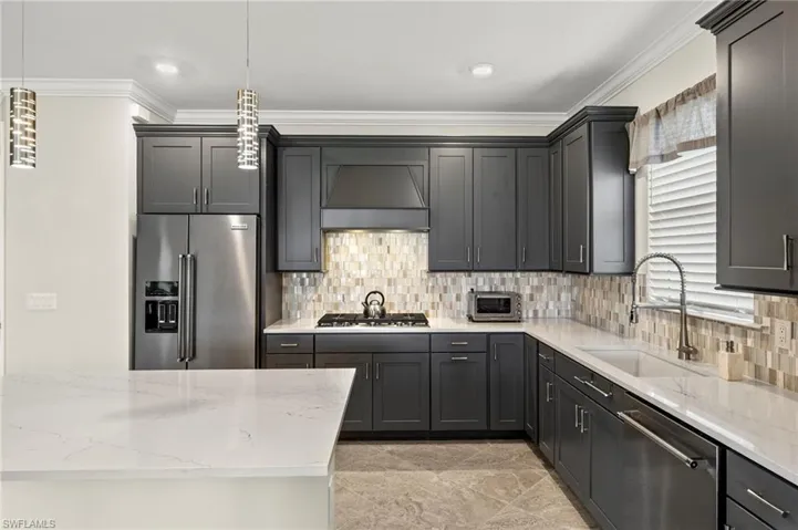 Kitchen featuring a sink, stainless steel appliances, crown molding, light stone countertops, and custom range hood