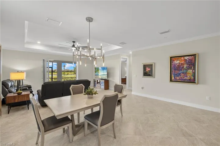Dining room with ceiling fan with notable chandelier, ornamental molding, visible vents, a raised ceiling, and baseboards