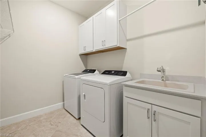 Laundry room with cabinet space, washer and clothes dryer, baseboards, and a sink