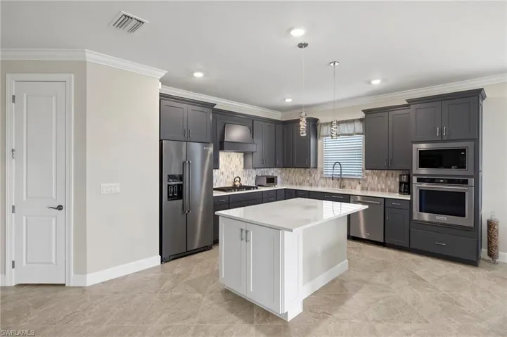 Kitchen with stainless steel appliances, ornamental molding, visible vents, wall chimney exhaust hood, and backsplash