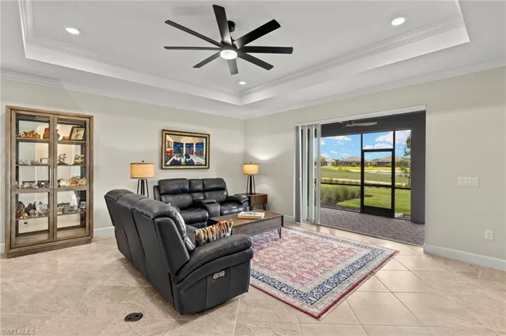 Living room with light tile patterned floors, a tray ceiling, crown molding, baseboards, and ceiling fan