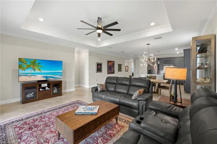 Living room featuring a tray ceiling, light tile patterned flooring, ceiling fan with notable chandelier, and baseboards