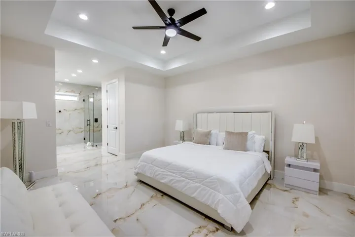 Spacious room featuring glossy marble-look flooring, a tray ceiling with recessed lighting, and a dark-toned ceiling fan