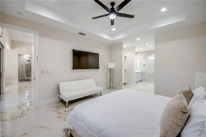 Spacious room featuring large format marble-look tile flooring, tray ceiling with recessed lighting and a ceiling fan, and an open doorway leading to a bathroom with a dual vanity