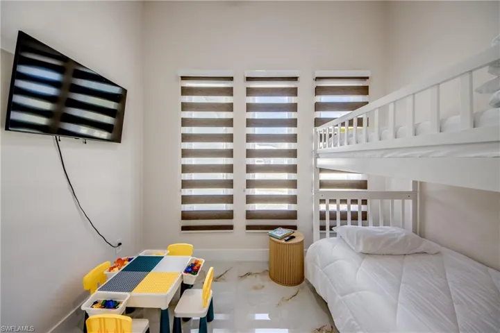 Spacious room featuring a white bunk bed, three windows with horizontal blinds, a wall-mounted television, and light-toned tile flooring