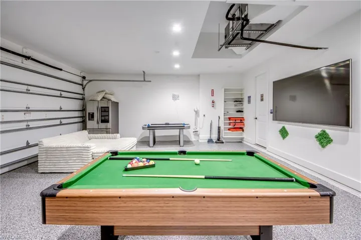 Recreation space featuring a wood-finish pool table, epoxy flooring, recessed lighting, a mounted display, and a white overhead garage door