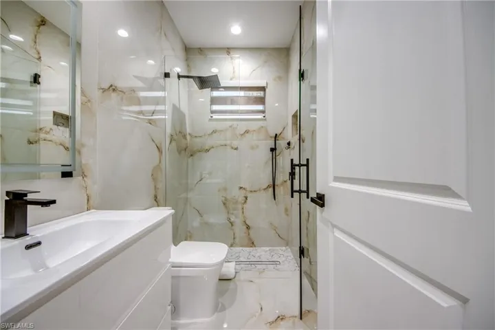 Contemporary bathroom featuring a frameless glass shower enclosure with matte black hardware, a rainfall showerhead, and a built-in niche