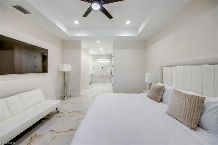 Spacious bedroom featuring elegant tray ceilings with recessed lighting, a modern ceiling fan, and large format marble-look tile flooring