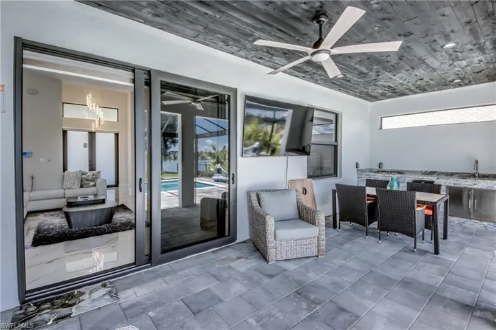 Spacious outdoor living area with a wood-plank ceiling, large ceiling fan, integrated outdoor kitchen with stainless steel cabinetry, and expansive sliding glass doors