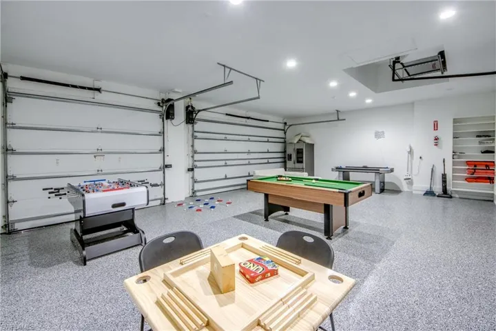 Spacious garage featuring a durable epoxy-coated floor, two overhead garage doors, recessed lighting, built-in shelving, and white painted walls