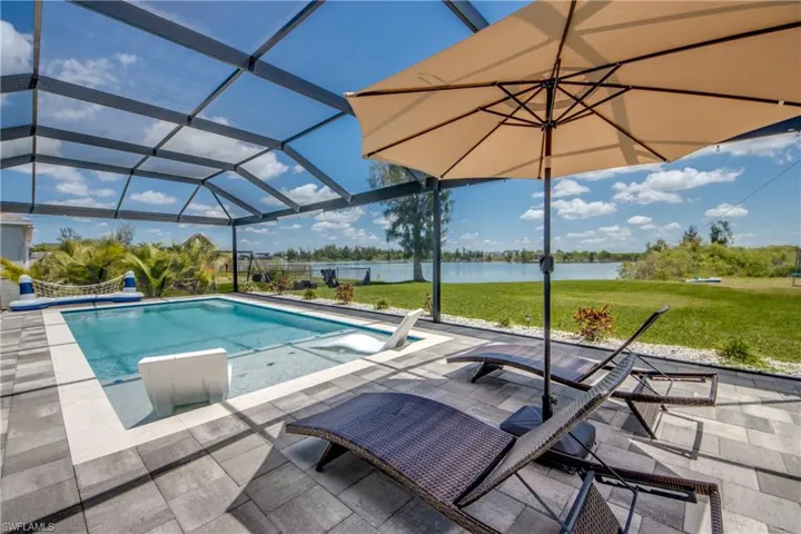 Screened-in outdoor living space featuring an in-ground swimming pool with an integrated sun shelf, extensive paver patio, and mature landscaping