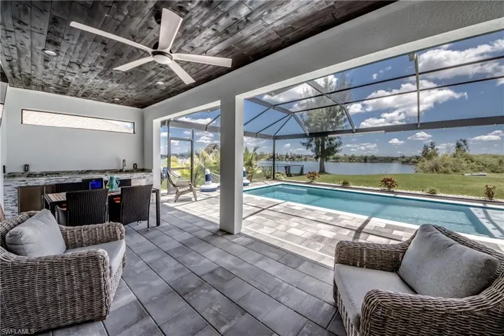 Spacious screened lanai featuring an outdoor kitchen, wood-finish ceiling, ceiling fan, and swimming pool with water views