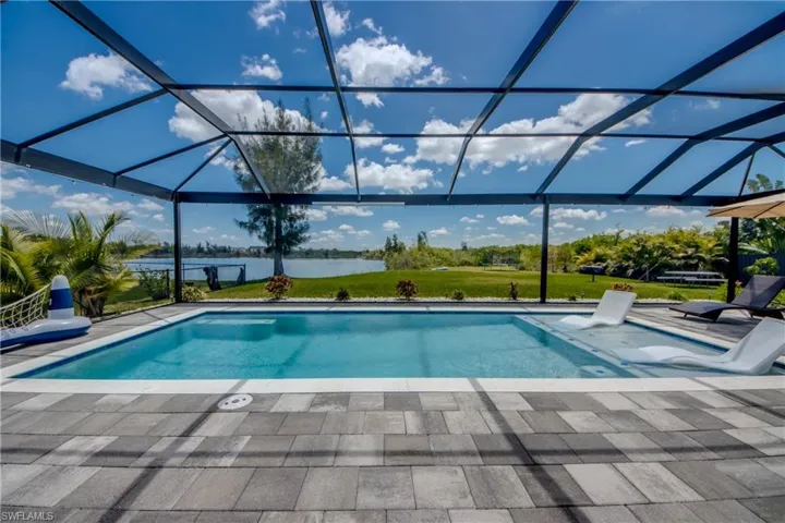 Screened lanai featuring a rectangular swimming pool with an integrated sun shelf, set within a paver patio