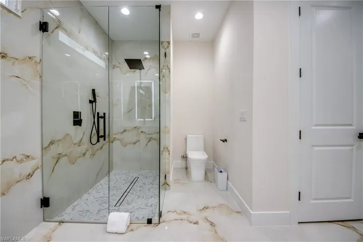 Glass-enclosed shower with matte black fixtures, integrated linear drain, and patterned floor tile