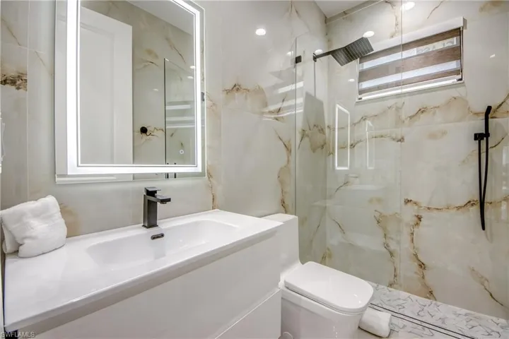 Contemporary bathroom featuring a floating vanity with integrated sink, an illuminated mirror, and a walk-in shower with a glass enclosure