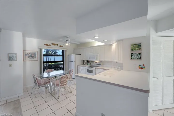 Kitchen with light countertops, a peninsula, light tile patterned floors, white appliances, and ceiling fan