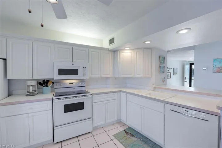 Kitchen featuring a sink, light tile patterned floors, white appliances, visible vents, and white cabinets