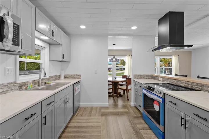 Kitchen featuring appliances with stainless steel finishes, range hood, a sink, baseboards, and light stone countertops